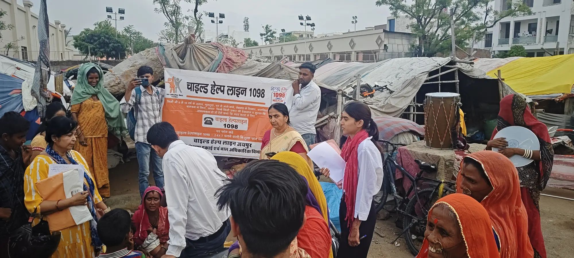Foundation volunteers speaking with families beside a Child Helpline 1098 banner during settlement outreach.
